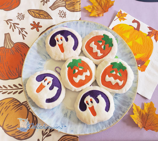 Plate with ghost and pumpkin cookie soft keychains. On a table with purple tablecloth, pumpkin table runner and pumpkin napkin.